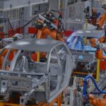 imagem de automotivo: linha de montagem de carros numa fábrica com braços mecânicos.